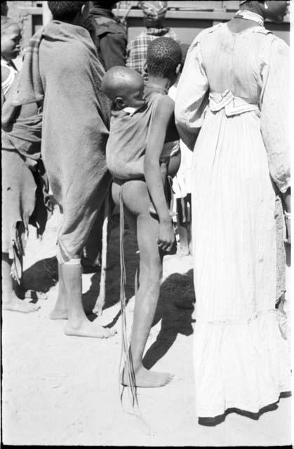 Girl with a baby tied to her back, standing next to a woman, view from behind