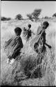 /Twikwe, DaSi!Na, and Tsekue carrying N!whakwe walking in grass