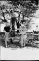 Laurence Marshall and an expedition member holding camera tripod while John Marshall films standing on top of a table
