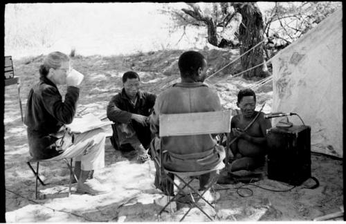 Oukwane playing the musical bow while Lorna Marshall, Kernel Ledimo, and Dabe record; Lorna Marshall drinking tea