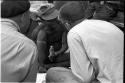 "/Gao Overalls" holding a bird with O.P.M. Prozesky and Nicholas England sitting across from him, seen from behind