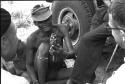 "/Gao Overalls" holding a bird with O.P.M. Prozesky and Nicholas England sitting across from him, seen from behind