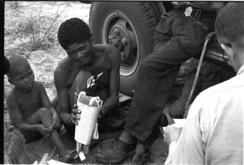 "/Gao Overalls" holding a bird sitting next to a boy with Nicholas England sitting across from him, seen from behind