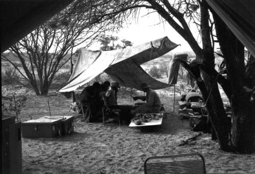 Four people sitting under a tent at camp