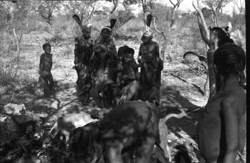 Group of people cutting up an ostrich with a group of women dancing in the background
