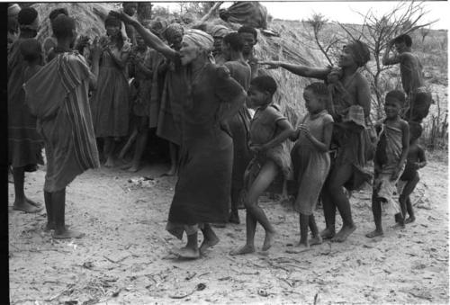 N//aba leading a group of girls, /Gishay holding eland horns in the background