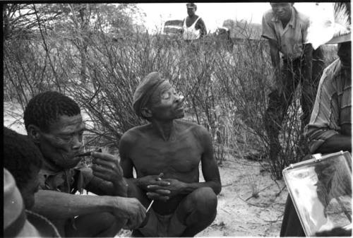 Wilhelm Camm in a chair with a sound recorder interviewing two men sitting on the ground