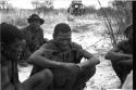 Four men sitting on the ground; truck in the background