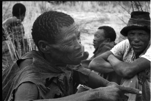 Man sitting and gesturing, four men sitting in the background