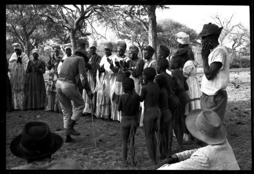 Group of women clapping, standing in a line with Judas Kangengi standing in the middle singing; people watching