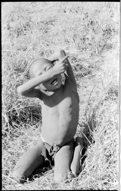 Child sitting on the ground with their arm over their eyes