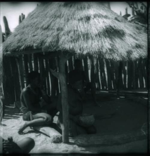 Women sitting and eating in the shade of a thatched roof