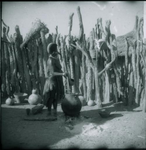 Woman stirring something in a large pottery cooking pot on the fire