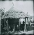 Person sitting next to a storage basket covered with a thatched roof