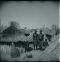 Two women and a child standing next to their huts