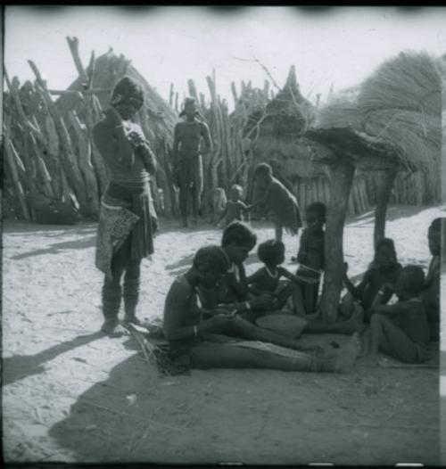 Girls sitting and working on a woven band with beads on it, and a woman standing next to them