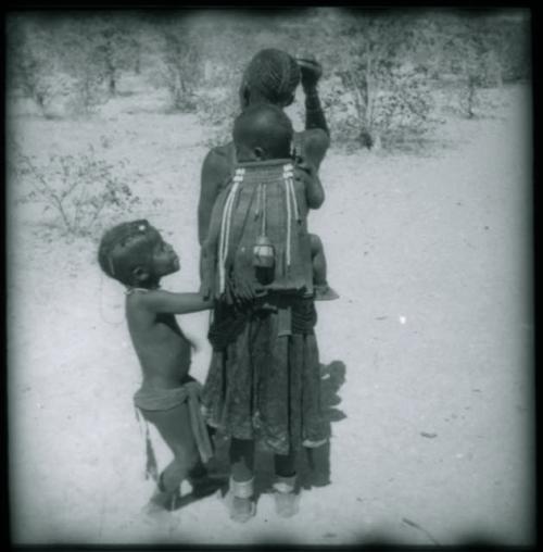 Woman carrying a child on her back, and another child standing next to her