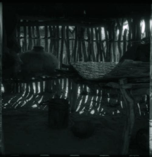 Woven mat, wooden bucket with leather handle, and large pot inside a storage hut