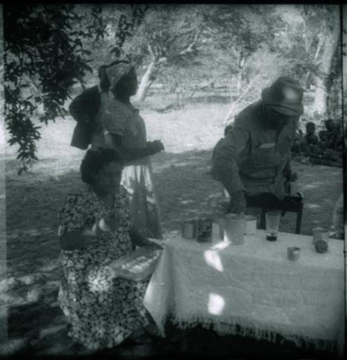 People standing and sitting at camp, with Mm. Simões seated at a table