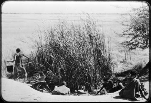 /Qui carrying an Ovambo pot full of water, with other people sitting and standing around a waterhole