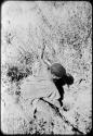 Woman digging, her digging stick in her left hand, pulling sand out of a hole with her right hand