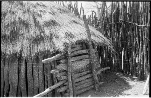 Storage hut with door; wall of wooden poles in the background