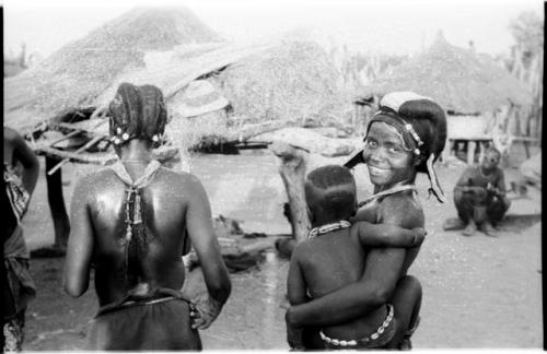 Two Hinga women; one woman is seen from behind and the other woman is holding a child and looking at the camera