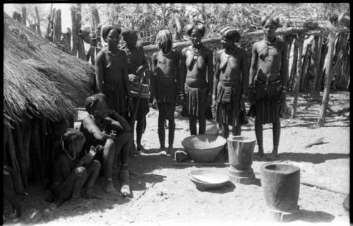 Hinga women and children by a hut with mortars and baskets by their feet