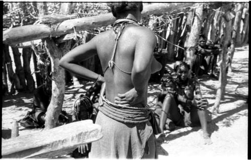 Woman, standing, seen from behind, and other seated women in the background