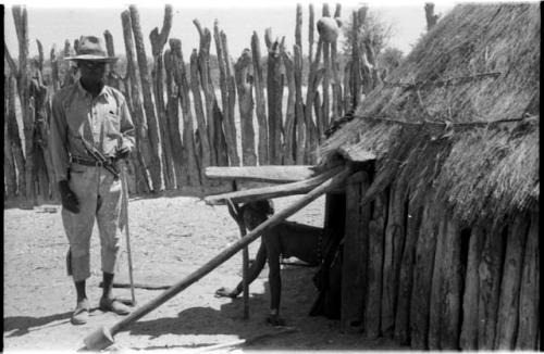 Man wearing Western clothing and a woman emerging from a hut's low doorway