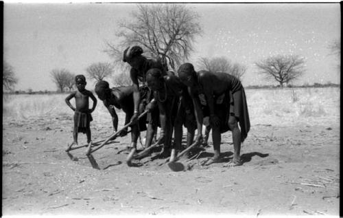 Four women using hoes, children behind them