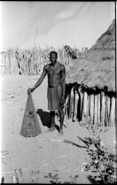 Man standing by a hut and holding a fish basket