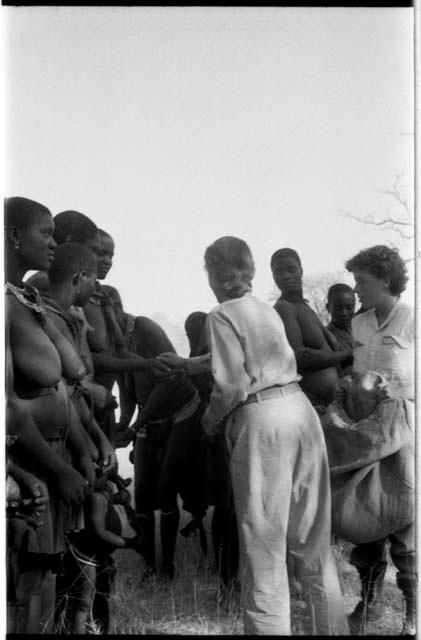 Lorna Marshall and Elizabeth Marshall Thomas talking to a group of women and children and giving them tobacco