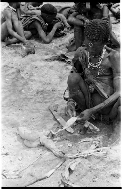 "Old Xama" preparing a piece of skin, other unidentified people in the background