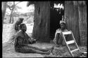 Three women sitting in front of a hut