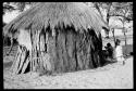 Woman and another person sitting beside a hut, seen from a distance