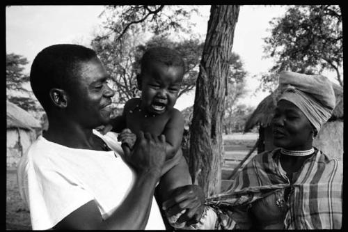 Edward Mutihimuno, Philip Hameva's assistant cook, holding a baby; a woman standing beside him