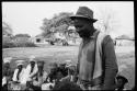 Kangengi standing and listening to Nick England play back recordings; women sitting in the background