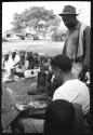 Judas Kangengi standing listening to Nick England playing back recordings, women sitting in the background