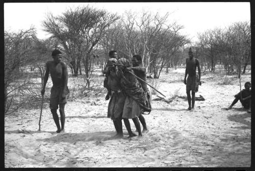 Tomku, /Gaishay, and a group dancing, /Gaishay's arms over Tomku and another woman; people sitting to the side
