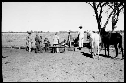 Expedition members standing by a water trough; man with two horses