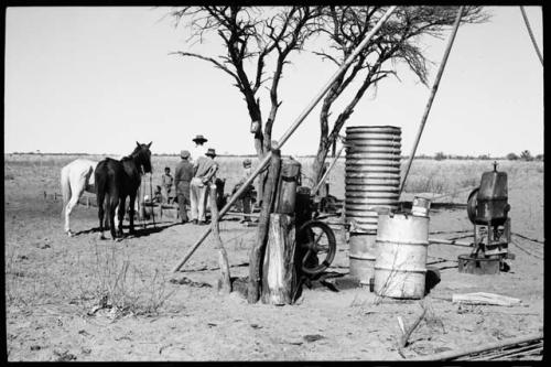 Expedition members standing by a water trough; man with two horses