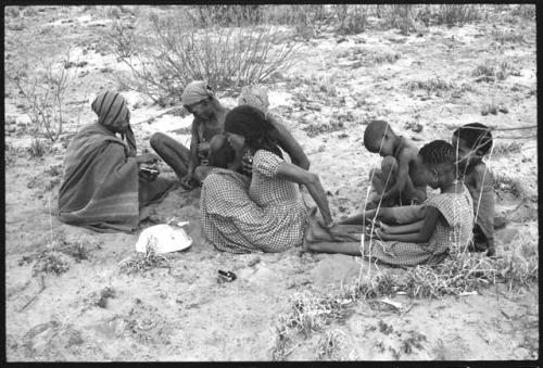 N/kxabe; Tomku; Dadum; and ǂKxoba sitting and playing a dandiri; three children sitting to the side