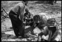 Ngani and Lorna Marshall bending over Xama, treating her leg; person sitting and watching them