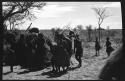 Group of people performing the Eland Dance; group of women clapping; men holding wooden horns to their heads