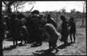 Group of people performing the Eland Dance; group of women clapping; men holding wooden horns to their heads