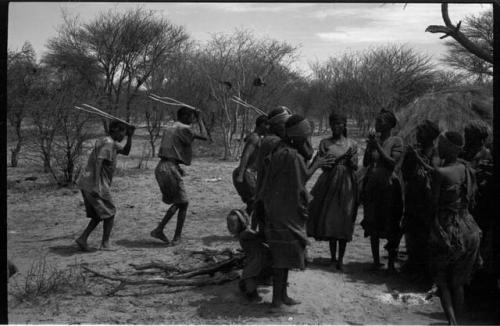 Group of people performing the Eland Dance; group of women clapping; men holding wooden horns to their heads