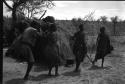 Group of people performing the Eland Dance; !Ani leading a line of people, man holding wooden horns to his heads
