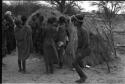 Group of people performing the Eland Dance; group of women clapping; man with wooden horns strapped to his head