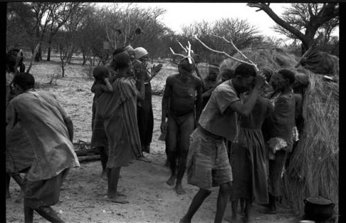 Group of people performing the Eland Dance; group of women clapping; men with wooden horns on their heads
